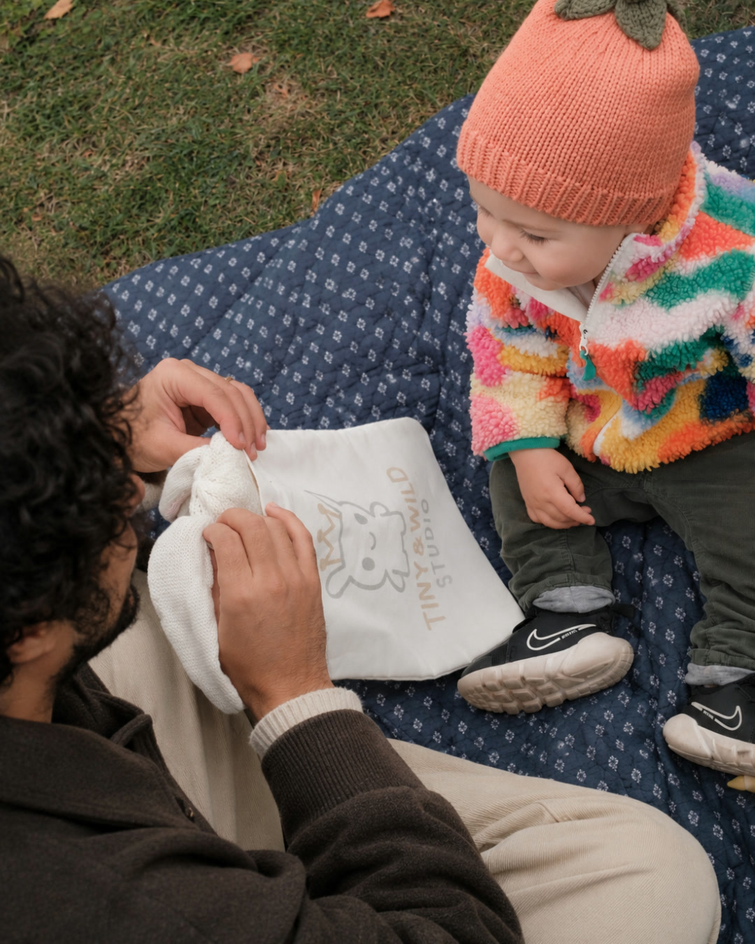 Parent opening a Tiny & Wild fabric gift bag beside a baby wearing the Pumpkin beanie