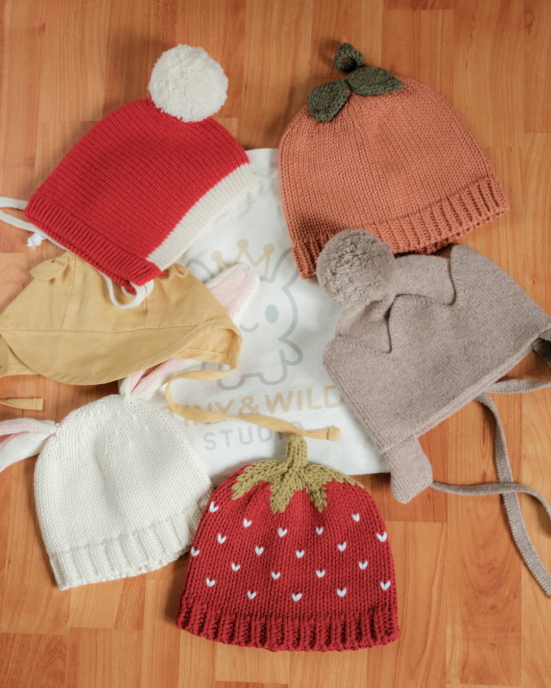 Six seasonal Tiny & Wild pieces arranged around a fabric gift bag on a wooden floor