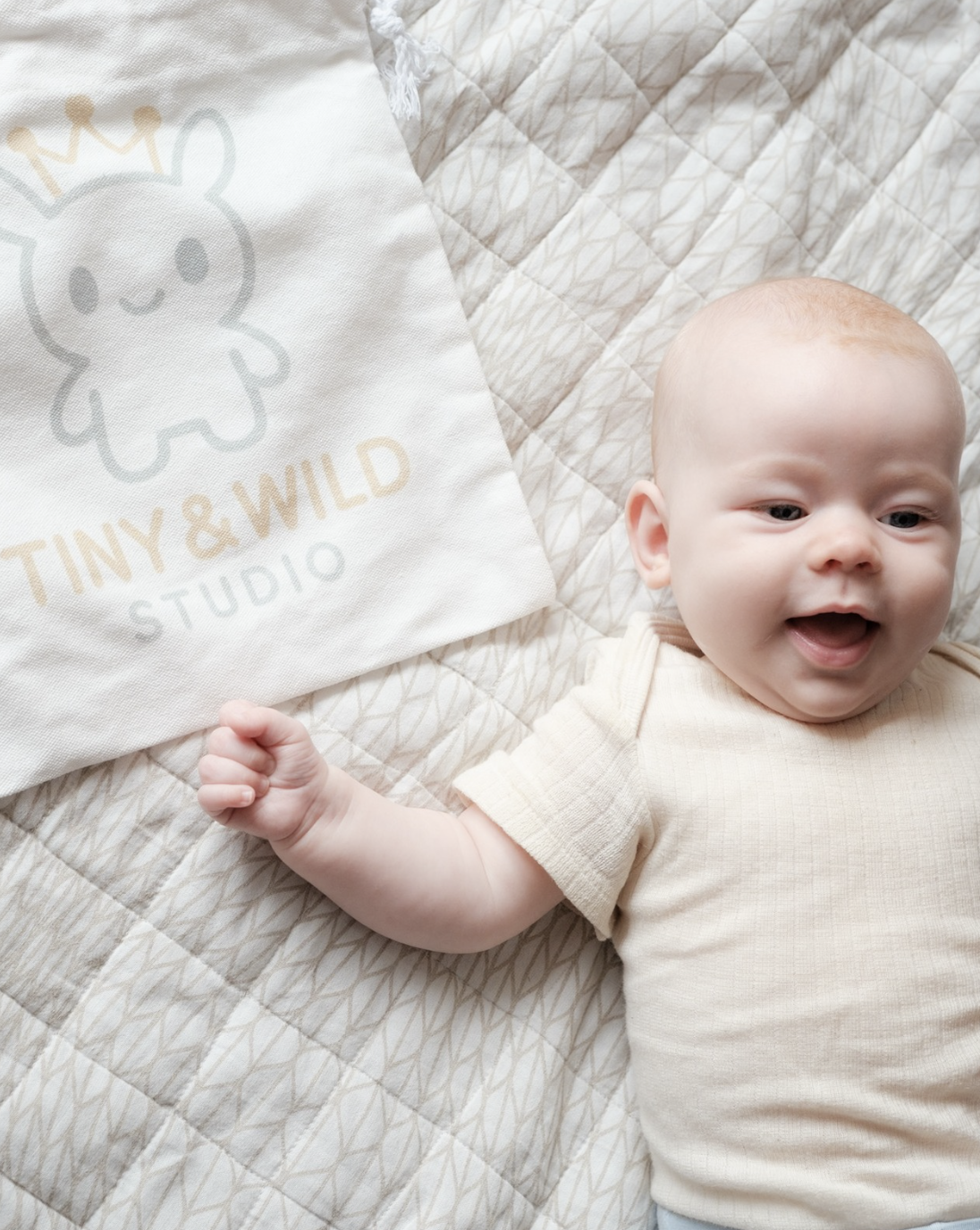 Smiling baby lying beside a Tiny & Wild fabric gift bag