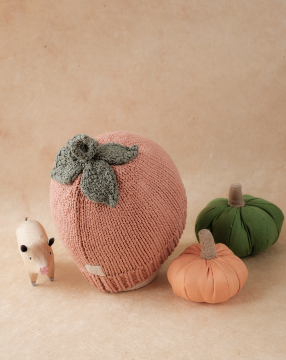 Pumpkin beanie displayed with soft fabric pumpkins and a small animal figurine