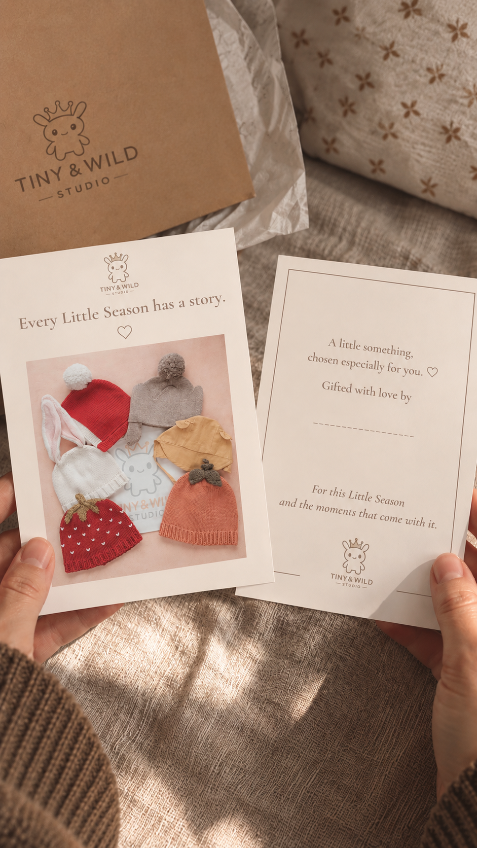 Des mains tiennent des cartes de collection et de message cadeau Tiny & Wild à côté d’un emballage cadeau en papier kraft