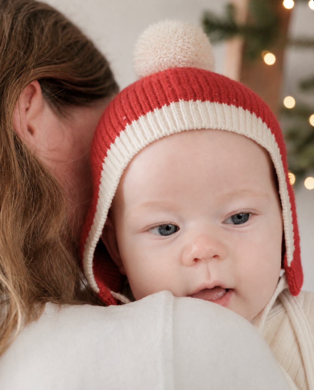 Baby wearing the red and cream Christmas Beanie while resting on a parent’s shoulder
