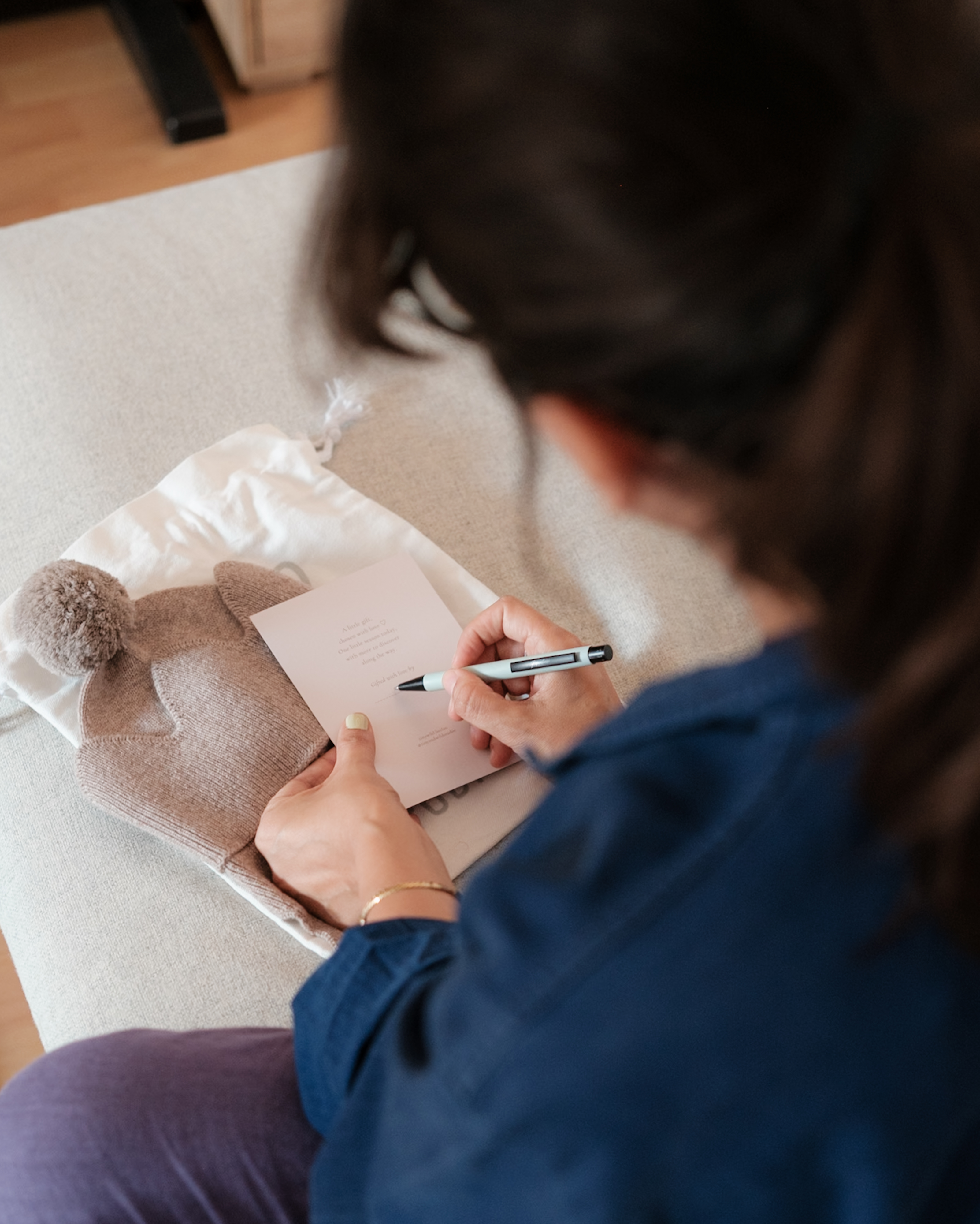 Person writing a gift card beside a Crown beanie and a Tiny & Wild fabric gift bag