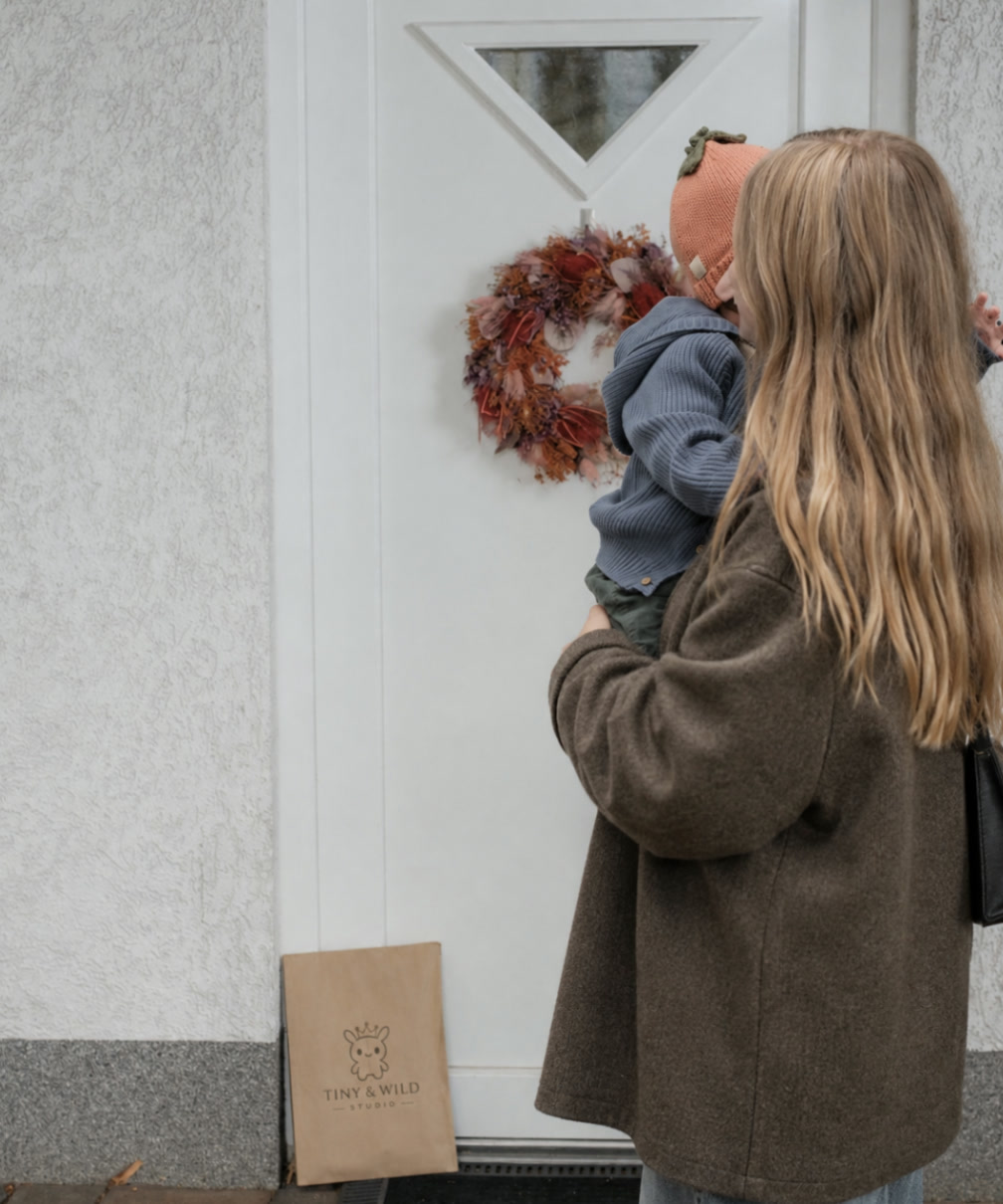 Parent and baby wearing the Pumpkin beanie arriving at a front door with a Tiny & Wild gift waiting